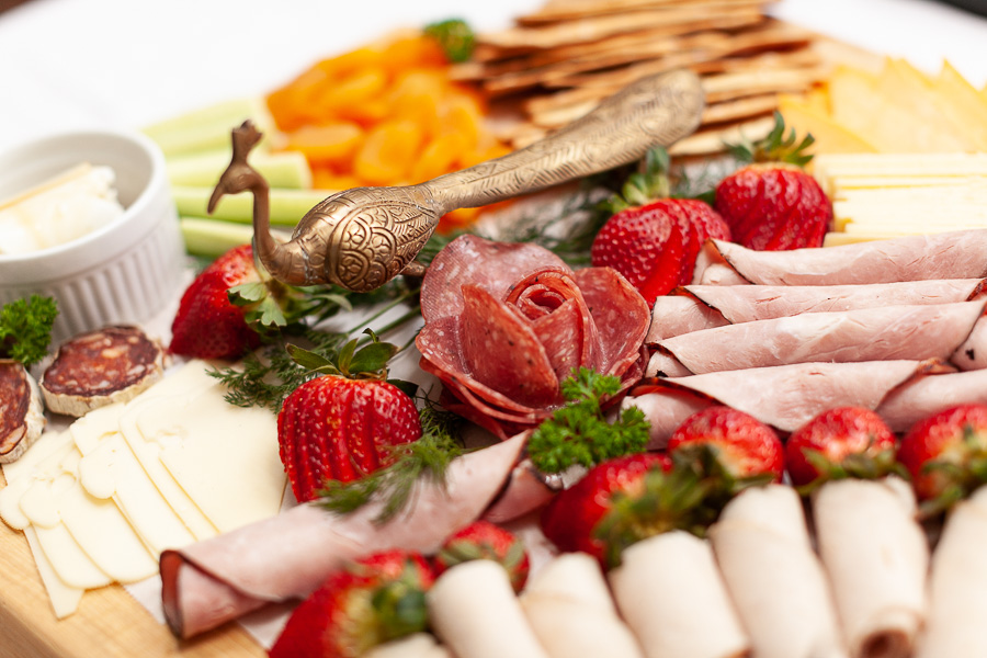arrangement of deli meat, cheese and fruit on a wood charcuterie board