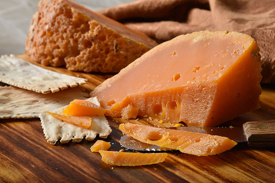 Mimolette cheese wedge on a dark a wood cheese board