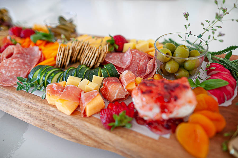 assorted cheese, meat, fruit and crackers on a wood charcuterie board
