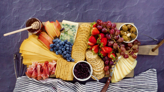 charcuterie board with cheese, crackers, honey, fruit and prosciutto