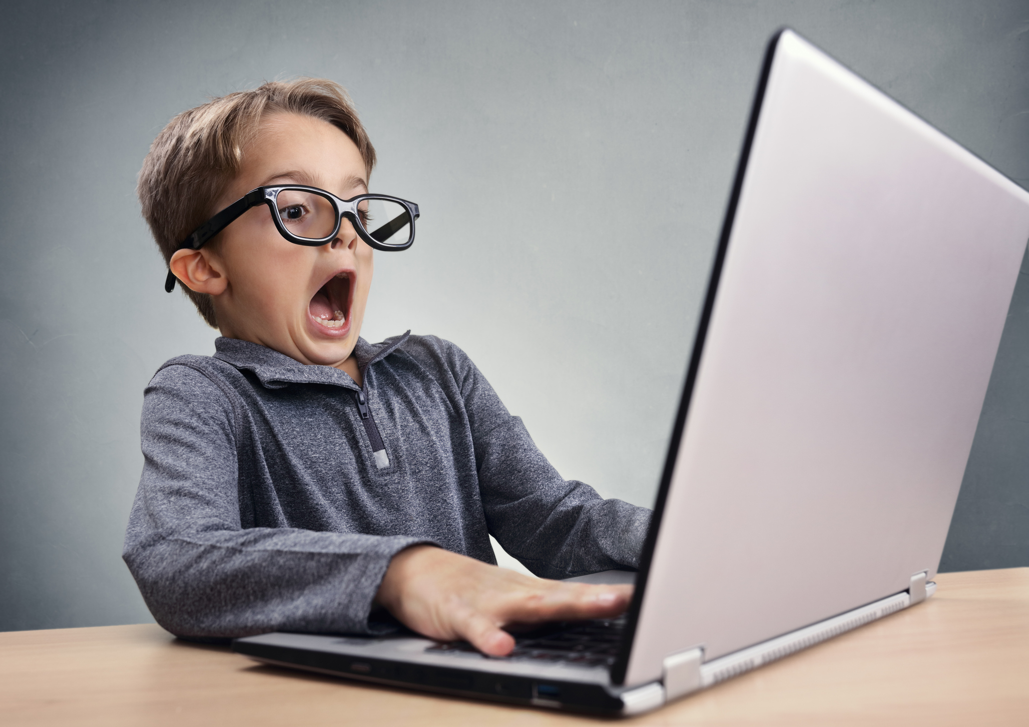 young boy with black glasses using a laptop computer at a desk